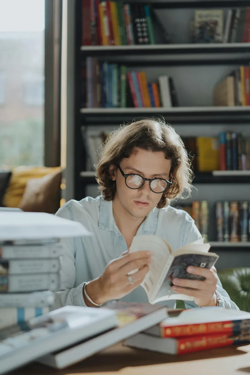 A young man reading a book in a cozy bookstore surrounded by shelves of books